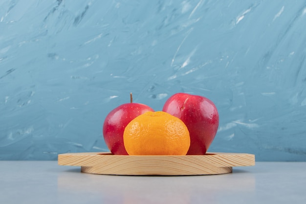 Free photo red apples and tangerine on wooden plate