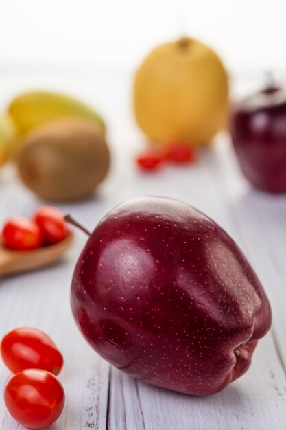 Red apples and tomato placed on the wooden floor.