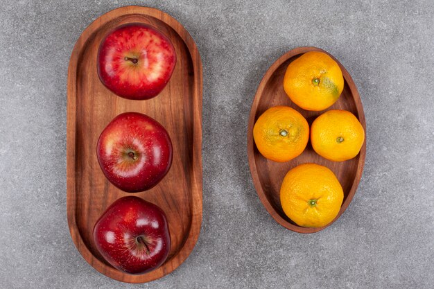 Red apples with sweet tangerines on a wooden board