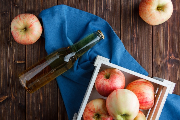 Free photo red apples in a wooden box and around with apple juice top view on a blue cloth and wooden background