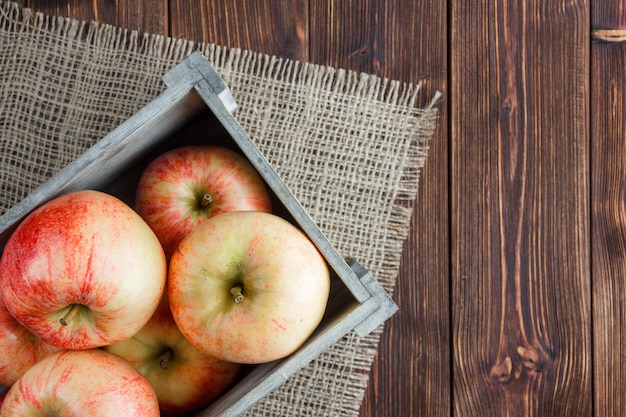 Free photo red apples in a wooden box top view on a sackcloth and wooden background space for text