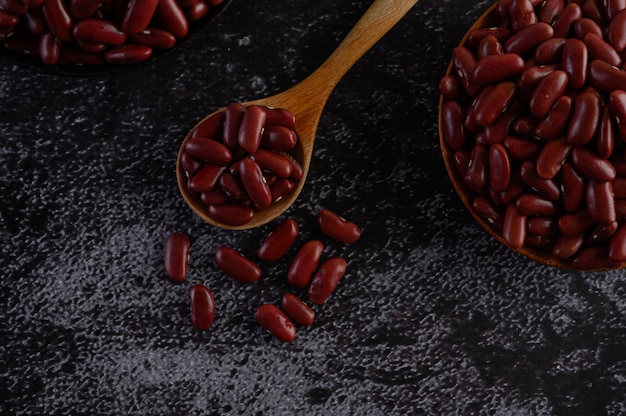 Free photo red beans in a wooden bowl and wooden spoon on the black cement floor.