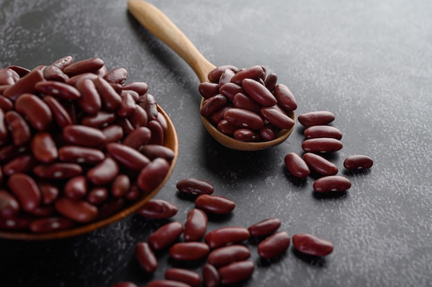 Free photo red beans in a wooden bowl and wooden spoon on the black cement floor.