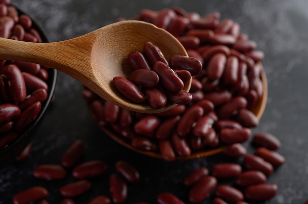 Free photo red beans in a wooden bowl and wooden spoon on the black cement floor.