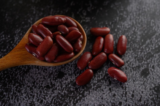 Free photo red beans in a wooden spoon on the black cement floor.