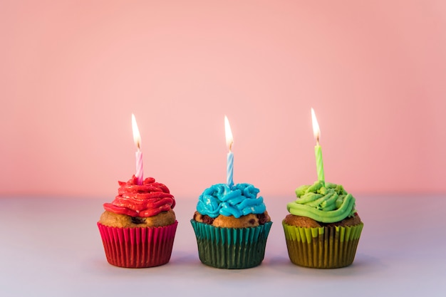 Free photo red; blue and green cupcakes with an lighted candles against pink backdrop