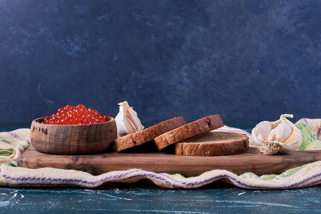 Red caviar on wooden board with bread slices.