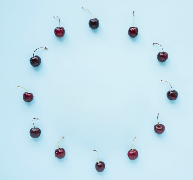 Free photo red cherries arranged in circular frame on blue background