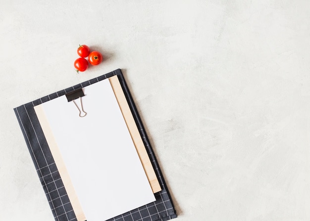 Free photo red cherries tomatoes and clipboard with white blank paper