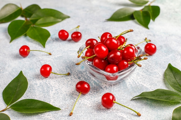 Red cherries in transparent glass bowl on gray table