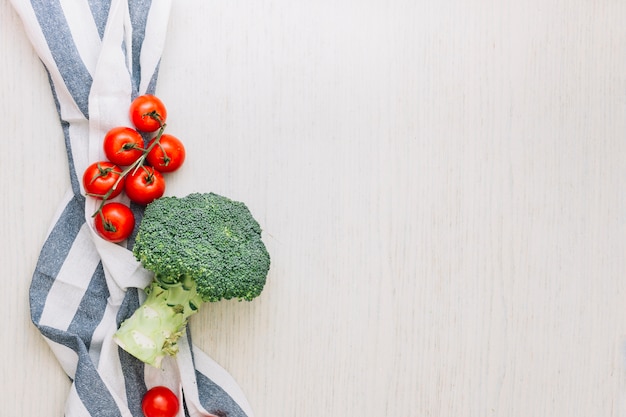 Free photo red cherry tomatoes and broccoli over the towel against wooden surface