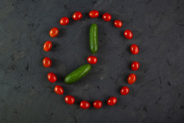 Red cherry tomatoes and green cucumbers on dark background