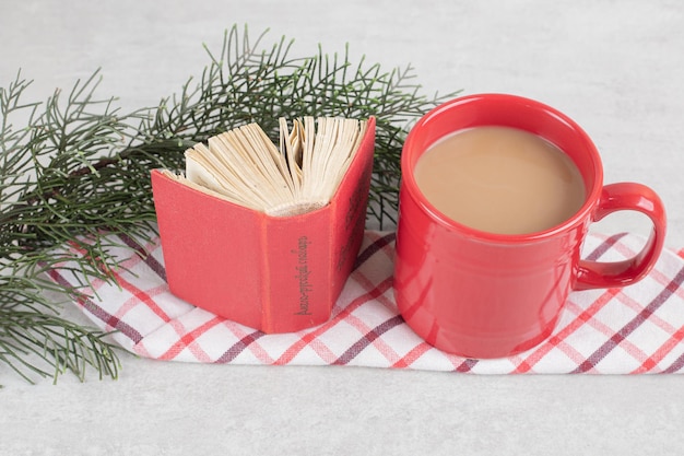 Red cup and book on tablecloth with pine branch