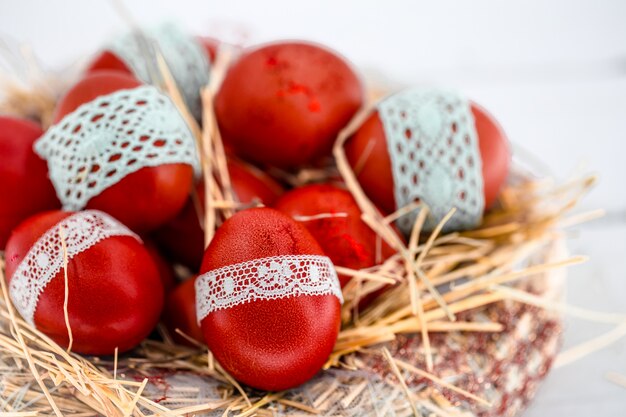 Red Easter eggs in a nest of hay, tied a lace ribbon, close-up, lying on a white wood