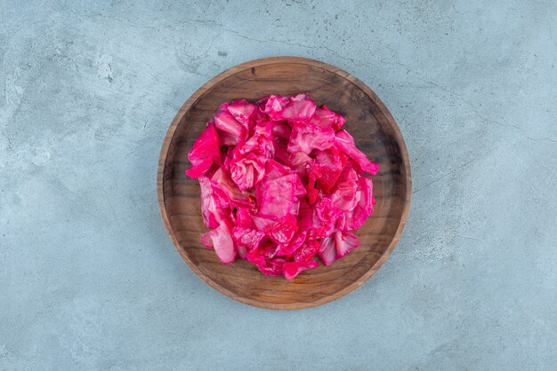 Red fermented sauerkraut on a wooden plate on the blue surface