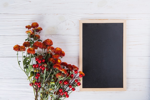 Red flowers with blank chalkboard on wooden table