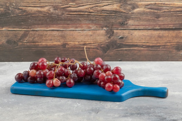 Free photo red fresh grapes placed on blue cutting board.