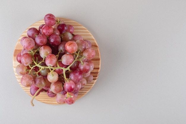 Red grape clusters on a wooden platter on marble 