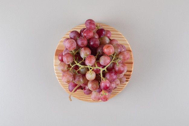 Red grape clusters on a wooden platter on marble 