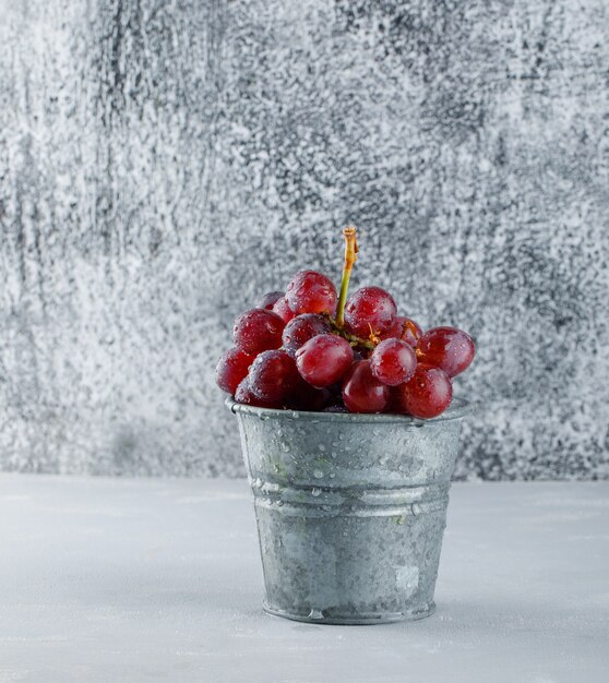 Red grapes in a mini bucket on plaster and grungy.