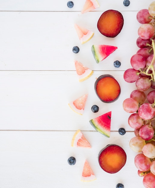 Red grapes; triangular slices of watermelon; grapefruits and blueberry on wooden desk