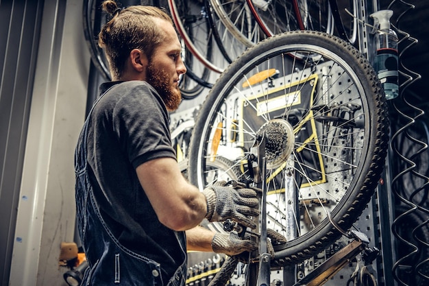 Red hair bearded mechanic removing bicycle rear cassette in a workshop.