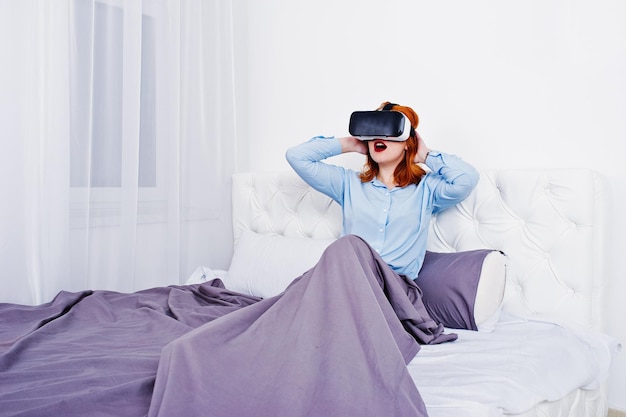 Free photo red haired girl in bed with vr glasses at studio room