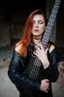 Free photo red haired punk girl wear on black with bass guitar at abadoned place portrait of gothic woman musician