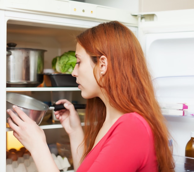 Free photo red-haired woman looking for something in fridge