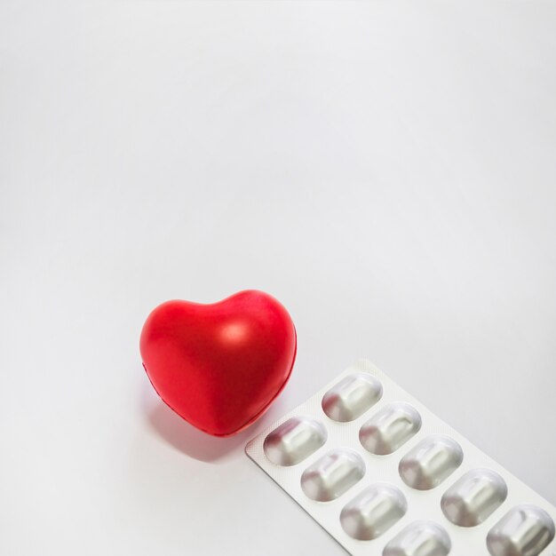 Red heart with silver packed pills on white background