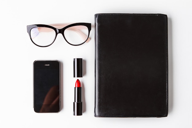 Red lipstick glasses phone and notebook over white background