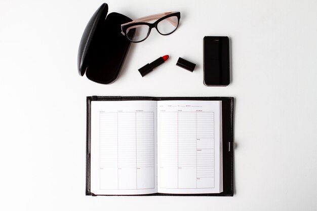 Red lipstick phone glasses and notebook over white background