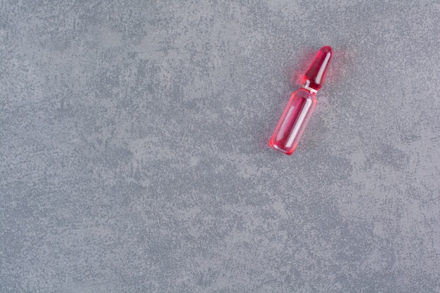 Red medical ampoule on marble table.