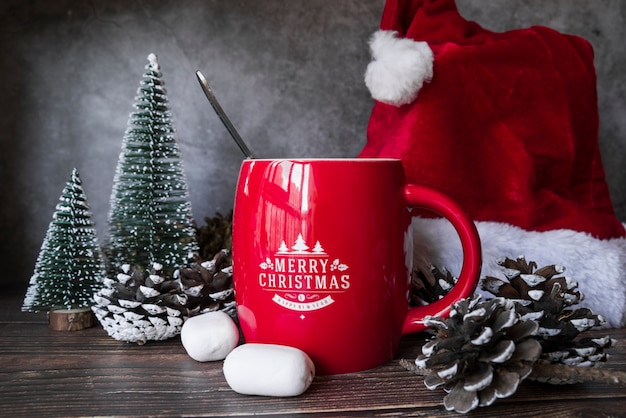 Free photo red mug near christmas hat and little fir trees