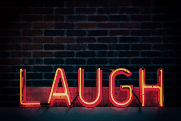 Red neon sign that says "LAUGH" on a dark brick wall background