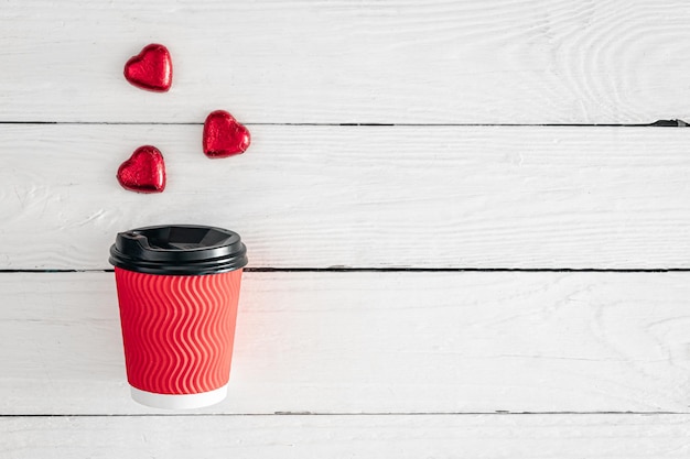 Free photo red paper cup and heartshaped candies on a white wooden background