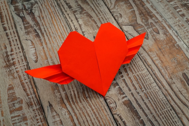 Free photo red paper origami heart with wings on wood background .