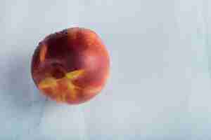 Free photo a red peach on white surface with water drops on it