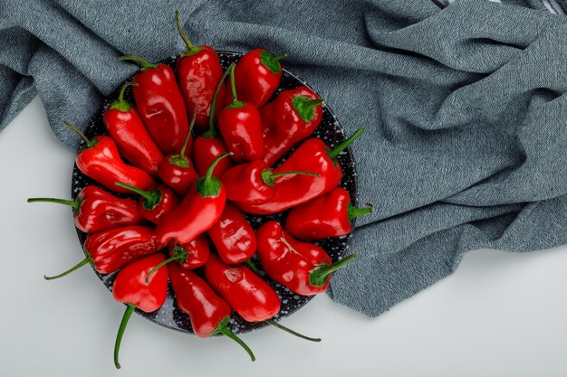 Red peppers in a plate flat lay on white and textile wall