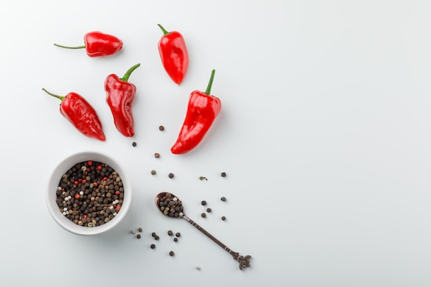 Red peppers with peppercorns in spoon and plate top view on a white wall