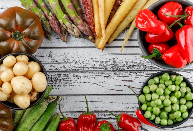 Red peppers with potatoes, tomatoes, asparagus, green pods, peas, carrots in a bowl on wooden wall, top view.