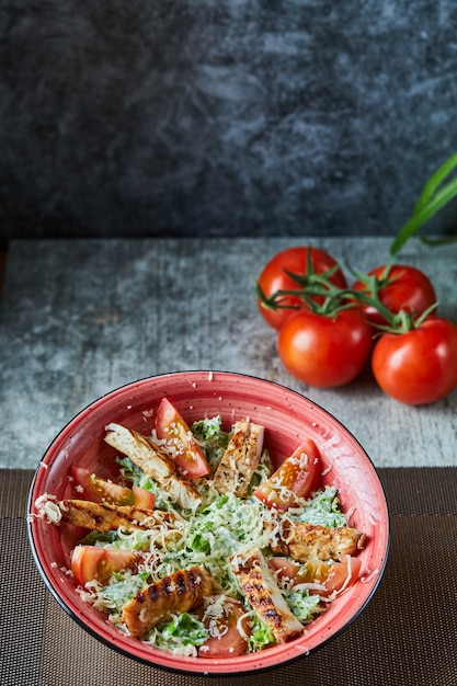 Free Photo a red plate with caesar salad and tomatoes in the marble surface