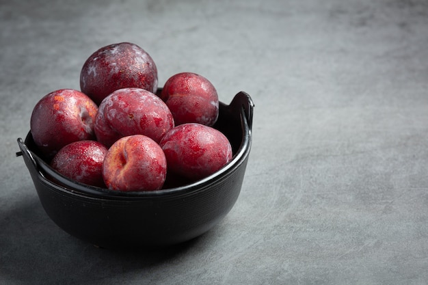 Red plum put in black bowl on dark floor