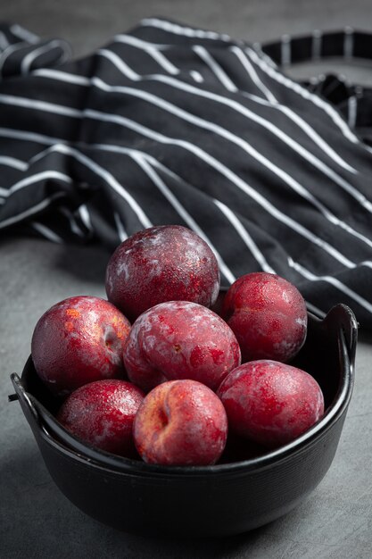 Free Photo red plum put in black bowl on dark floor