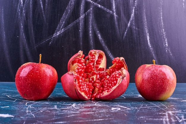 Free photo red pomegranate seeds and apples on blue space.