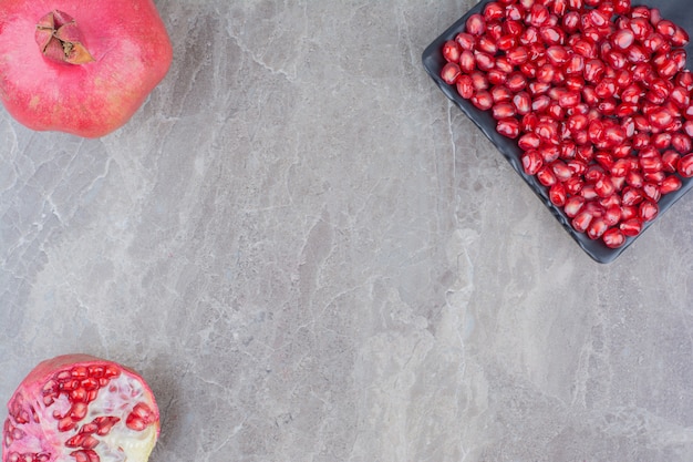 Red pomegranates and plate of seeds on stone background. 