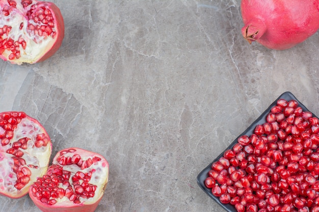 Red pomegranates and plate of seeds on stone background. 