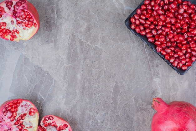 Red pomegranates and plate of seeds on stone background. 