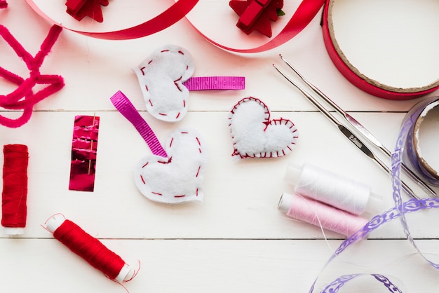 Red and purple ribbon; spools; crochet needle and heart shape on white plank