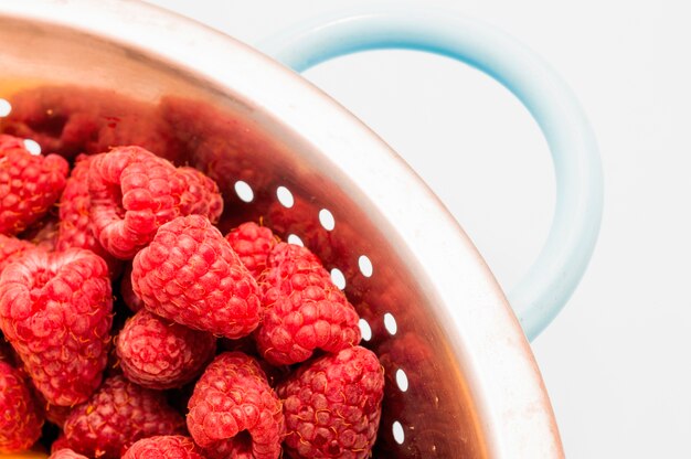 Red raspberries in stainless steel colander against white backdrop